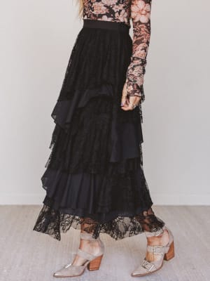 Person wearing a black lace skirt with floral top and metallic shoes on a neutral background