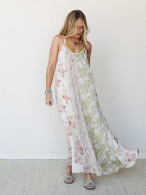 A flowy, patchwork floral maxi dress in cream and sage green panels catches mid-movement against a clean white wall — soft, romantic, and the kind of dress that makes you want to open a window.
