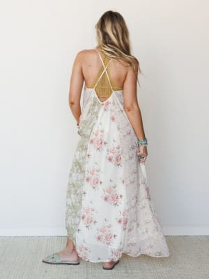 A flowy floral maxi dress shot from the back, showing off a crocheted mustard bodice with a strappy crossback detail — the kind of dress that makes you want to book a flight somewhere warm.