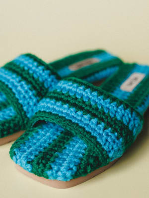 A pair of chunky crochet slide sandals in bold blue and green stripes, shot close up against a soft cream background — the kind of shoes that make a whole outfit feel more interesting without trying.