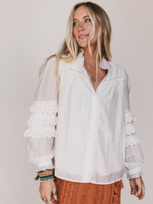 Woman wearing a white blouse with lace details on a plain background