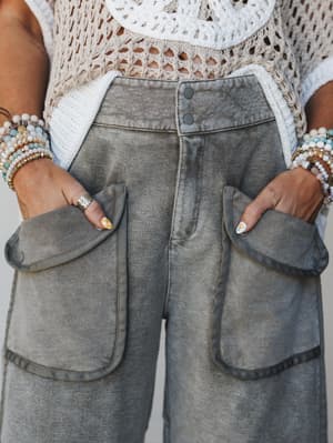 A close-up detail shot of washed olive barrel pants styled with a crochet crop top — hands tucked into oversized patch pockets, stacked beaded bracelets and a silver ring adding that perfectly layered, lived-in boho energy.