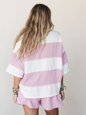 A back-view shot of a matching two-piece set — an oversized wide-stripe tee and relaxed shorts in orchid pink and ivory — styled with stacked boho bracelets for that effortlessly lived-in feel.