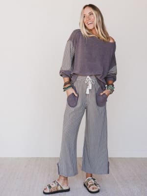 Woman wearing a purple off-shoulder top and striped pants against a white background