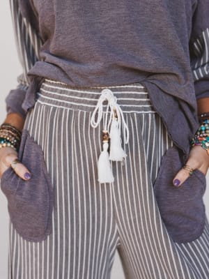 Person wearing a purple top and striped pants with tassel details.