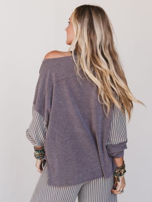 Person wearing a loose-fitting, off-shoulder top with long blonde hair on a plain background