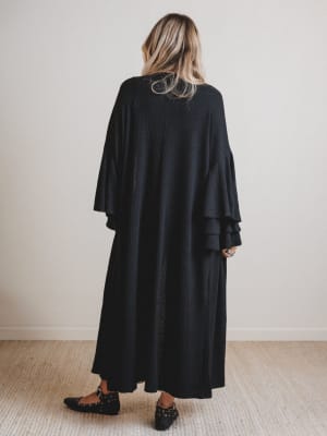 Woman wearing a black duster with ruffled sleeves in a minimal indoor setting