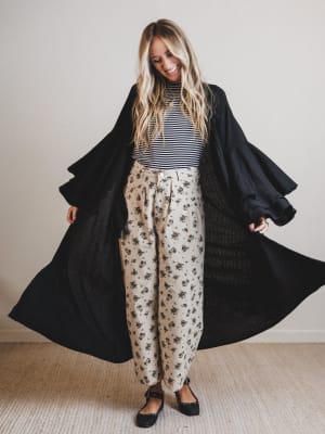 Woman wearing a black duster, striped shirt, and floral pants on a plain background
