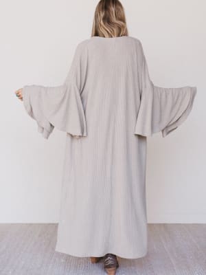 Person wearing a long, light gray ribbed dress with wide sleeves on a white background