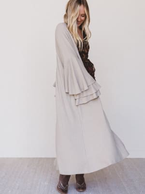 Woman wearing a long beige coat over a patterned dress against a white background