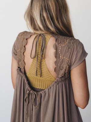 A close back-detail shot of a mocha dress with intricate floral embroidery and an open back, revealing a mustard yellow lace bralette underneath — the kind of layered, effortless detail that makes a dress worth turning around for.