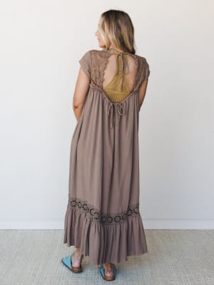 Shot from behind, this flowy mocha maxi dress does the quiet work of an outfit that knows it's special — open back with crochet floral cutout detail, a mustard yellow crochet inset panel, and a tiered ruffle hem with matching floral lace trim, worn w