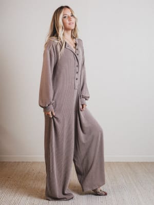 Woman wearing a brown jumpsuit standing against a plain background