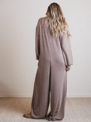 Person wearing a brown jumpsuit standing against a plain white wall.