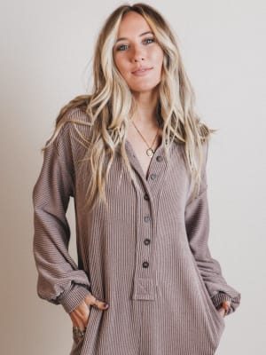 Woman wearing a long, brown ribbed dress with a button-up front against a plain background