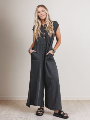 Woman wearing a dark gray jumpsuit standing against a plain background