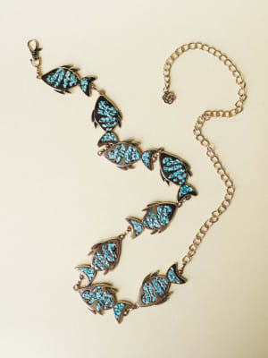 A gold chain belt laid flat, featuring linked fish-shaped charms filled with crushed turquoise stone inlay — the kind of piece that looks like it wandered in from a vintage Southwest market and never left.