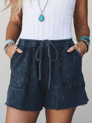 A mid-shot of acid-washed navy drawstring shorts paired with a white textured tank and layered turquoise jewelry — the kind of effortless summer outfit that looks put-together without trying.