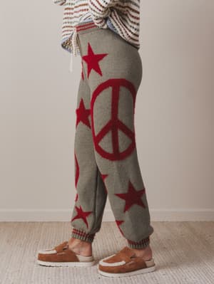 Gray knit pants with red peace signs and stars worn by a person indoors.
