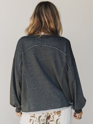 Person wearing a dark gray oversized sweater with white trim on a plain background
