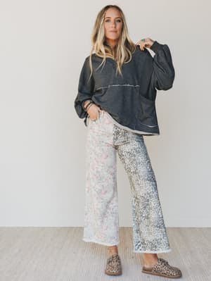 Woman wearing a dark gray oversized sweater and light-colored patterned pants against a white background