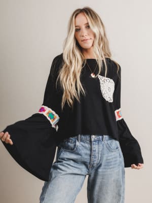 Woman wearing a black boho blouse with colorful sleeves and a pocket, standing against a plain background