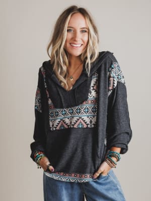 Woman wearing a dark gray hoodie with colorful tribal patterns on a plain background