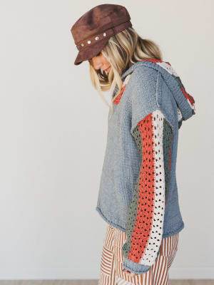 Woman wearing a denim jacket with colorful patchwork design and a brown hat.
