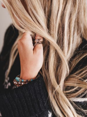 Close-up of a person's hand with a ring and bracelets, holding blonde hair.