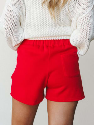 A back-view shot of cherry red pull-on shorts styled with a chunky open-knit cream sweater — casual and a little bold, the kind of outfit that works just as well for a weekend errand run as it does for a cozy night in.
