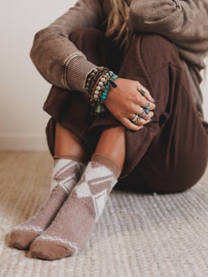 Person wearing brown sweater, pants, and argyle socks sitting on a carpeted floor.