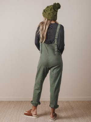 Person wearing green overalls and a matching beanie indoors.