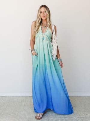 A flowy ombre maxi dress shifts from soft mint at the top to vivid cobalt blue at the hem, styled with a macramé fringe bag, stacked bracelets, and turquoise jewelry for an effortlessly boho summer look.