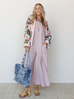 A full look styled around a wide-leg printed jumpsuit layered under a bold embroidered floral bomber, carried together with a ruffled denim tote — the kind of outfit that looks effortless but took exactly the right amount of thought.