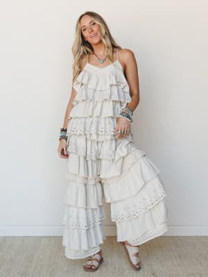 A tiered, ruffle-heavy maxi set in creamy taupe with eyelet and lace trim throughout — the kind of outfit that looks like it was made for wandering a coastal town with sandals and stacked bracelets.