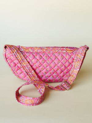 A quilted crescent-shaped crossbody bag in hot pink with a block-print floral pattern in peach and orange, photographed against a soft neutral background — the kind of bag that makes even a plain outfit feel intentional.