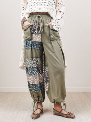 Person wearing a white crochet top and patchwork pants with a neutral background