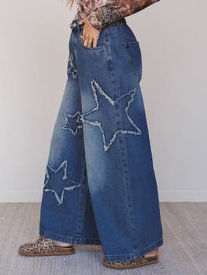 Wide-leg jeans with star patches worn by a person on a neutral background