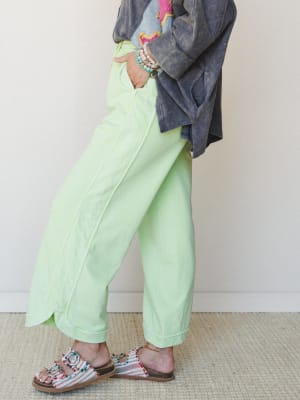 A cropped wide-leg pant in a soft lime green styled with an acid-wash embroidered jacket, beaded bracelets, and woven multicolor sandals — casual and expressive with a playful color punch.