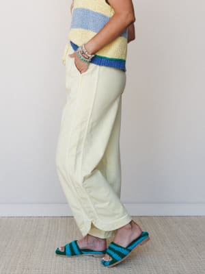 A side-profile shot of a model in butter yellow wide-leg pants paired with a color-blocked striped knit top and crochet slide sandals — the whole look has that easy, sunny energy of a good Saturday with nowhere to be.
