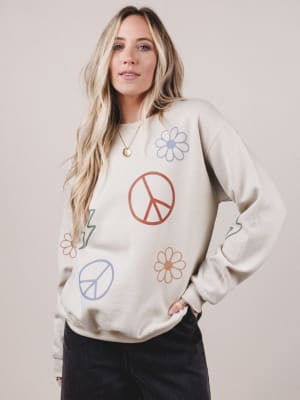 Woman wearing a cream-colored sweatshirt with peace signs and flowers on a plain background