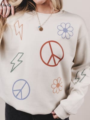 Person wearing a beige sweatshirt with peace signs, flowers, and lightning bolts.