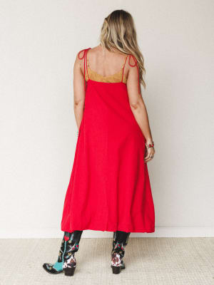 A bold red maxi dress with tie shoulder straps and a gold embroidered bodice, styled back-to-camera with statement embroidered cowboy boots — the kind of outfit that walks into a room before you do.