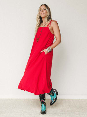 A flowy red maxi bubble dress with spaghetti tie straps and side pockets, styled with bold embroidered western boots and layered boho jewelry for a look that's equal parts free-spirited and statement-making.