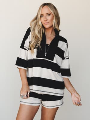 A relaxed striped short set with an oversized half-zip pullover and matching biker shorts, styled with layered gold necklaces and stacked rings — the kind of effortless matching set that works just as hard on a coffee run as it does on the couch.