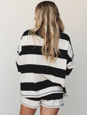 A back-facing shot of a relaxed stripe short set — oversized long-sleeve top and matching shorts in bold black and oatmeal stripes, with visible contrast stitching details that give it an easy, lived-in feel.