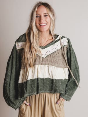 Woman wearing a green and beige layered sweater with a plain background