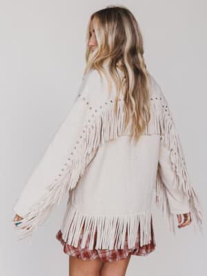 Woman wearing a white fringe jacket and plaid skirt on a plain background