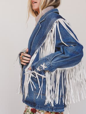 Blue denim jacket with white fringe on a plain background