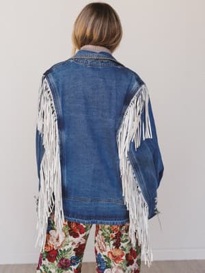 Person wearing a blue denim jacket with white fringe on a plain background